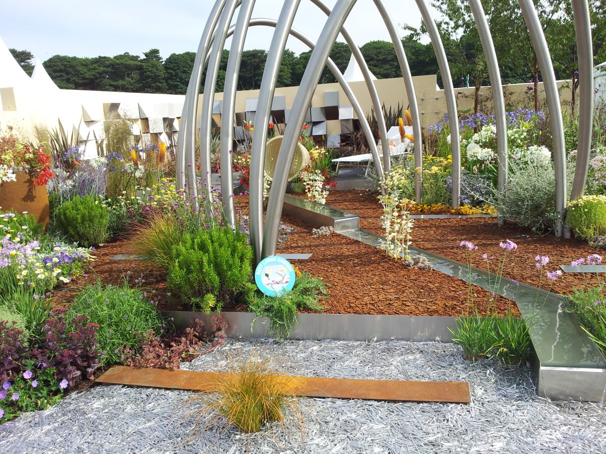 Stainless steel arches with water rill and stainless bed edging in a planted show garden
